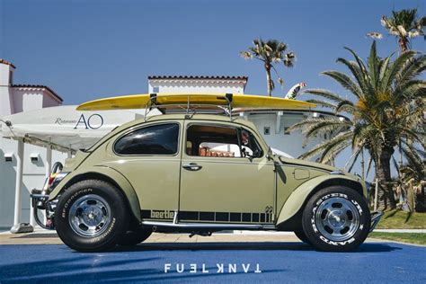 an old vw bug is parked in front of a building with surfboards on top