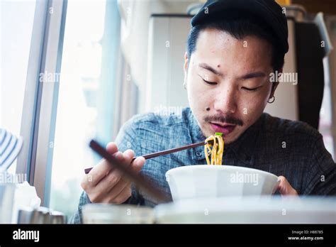 A ramen noodle cafe in a city. A man sitting eating ramen noodle soup ...