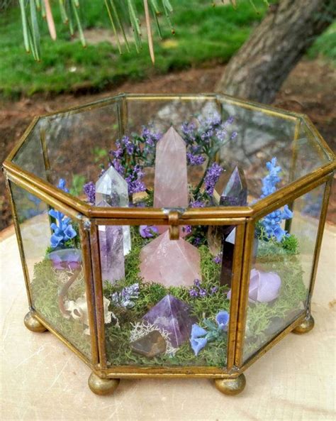 a glass box filled with rocks and flowers on top of a wooden table next ...