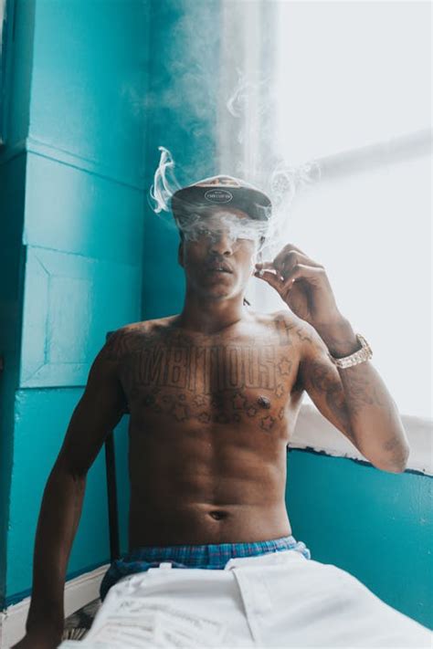 Tattooed Man Smoking Cigarette Near a Window · Free Stock Photo