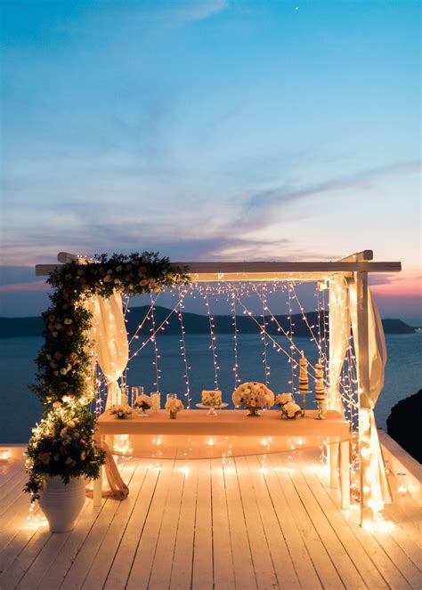 an outdoor wedding setup with lights and flowers on the deck at night, overlooking the ocean