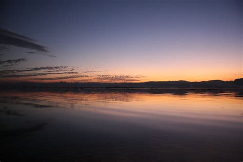 the sun is setting over water with mountains in the distance and clouds ...