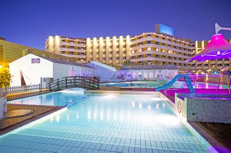 an outdoor swimming pool with water slide and hotel in the background ...