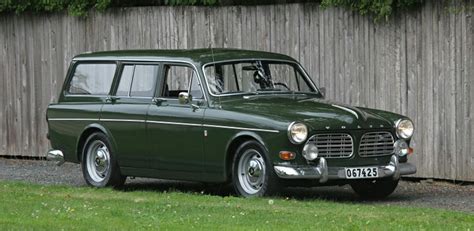 an old green station wagon parked in front of a wooden fence