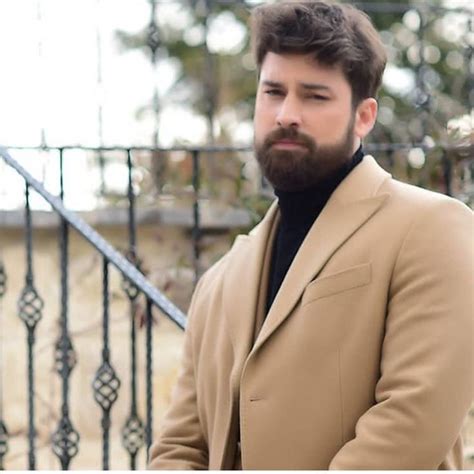 a man with a beard standing in front of a wrought iron stair railing and looking at the camera