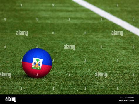 Haiti flag on ball at soccer field background. National football theme on green grass. Sports ...
