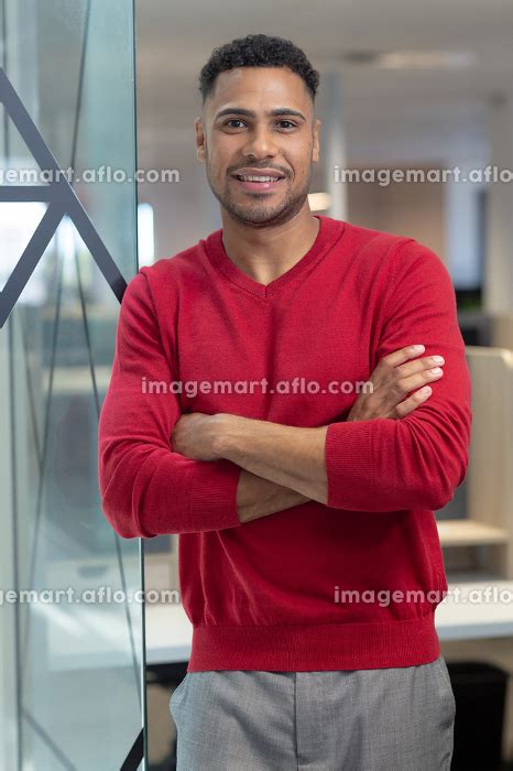 Portrait of smiling male hispanic professional with arms crossed standing at modern workplace ...