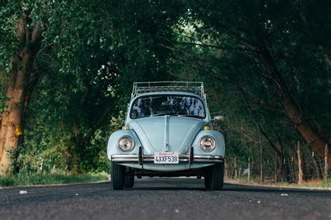 vintage blue volkswagen beetle parked on road in front of lake with mountains in the distance ...