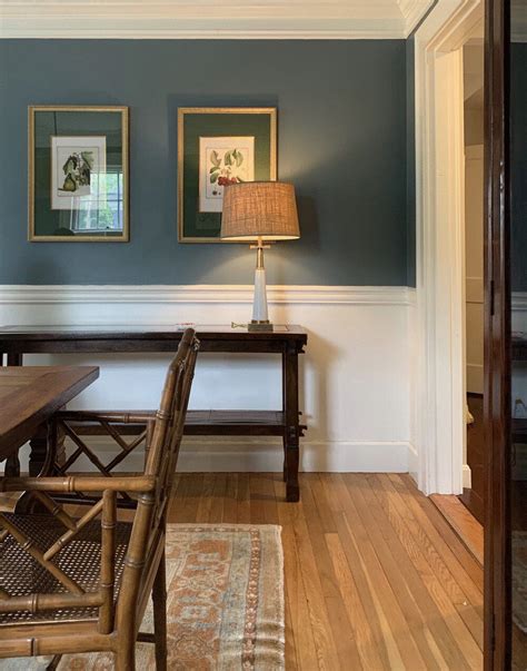 a dining room with blue walls and wood flooring is pictured in this image, there are two framed ...