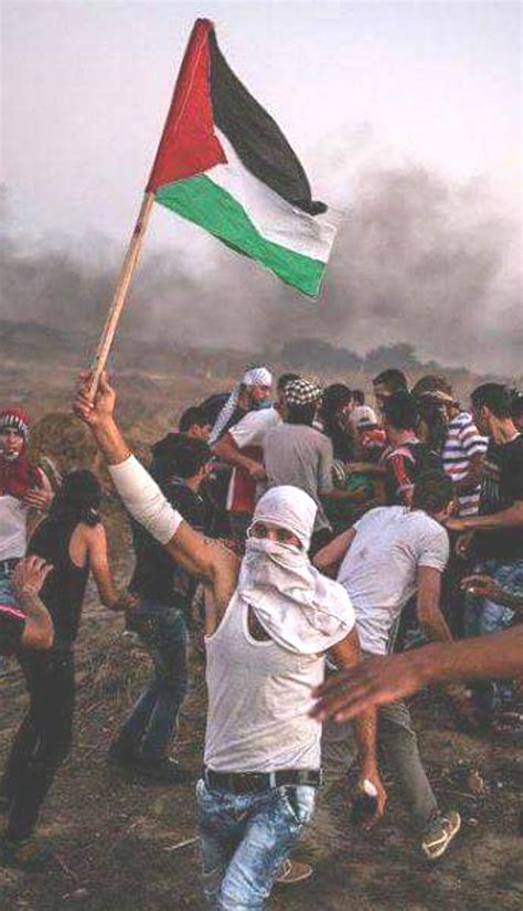 a group of people standing on top of a dirt field holding a flag in the air