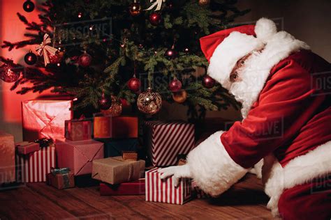 santa claus in traditional red costume putting gifts under christmas tree - Stock Photo - Dissolve