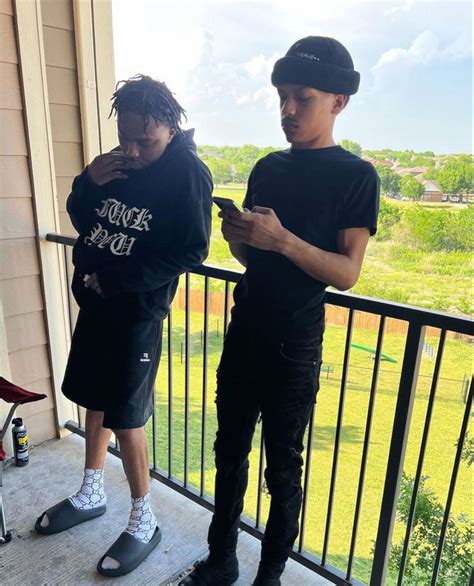 two young men standing on a porch looking at their cell phones while ...