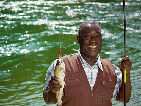 Black man holding fish and fishing rod near stream - Stock Photo - Dissolve