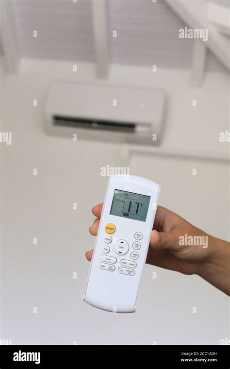 Young woman using a remote control of wall-mounted air conditioner ...