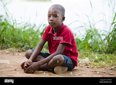 portrait of little boy sitting cross-legged alone in nature at the edge of a lake Stock Photo ...