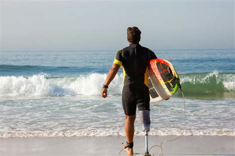 Unrecognizable male surfer amputee with surfboard walking towards sea ...