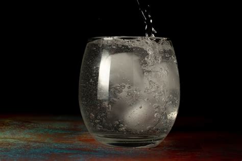Vaso de agua helada se llena con agua fría con gas sobre un fondo oscuro y superficie rústica ...