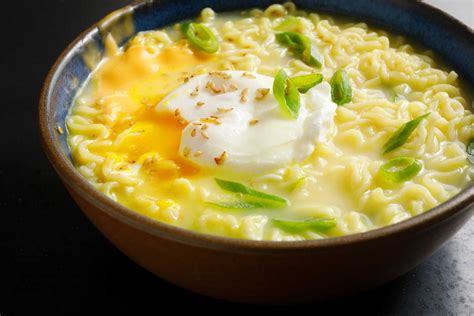 a bowl of noodles with sour cream and green onions on top is sitting on a table