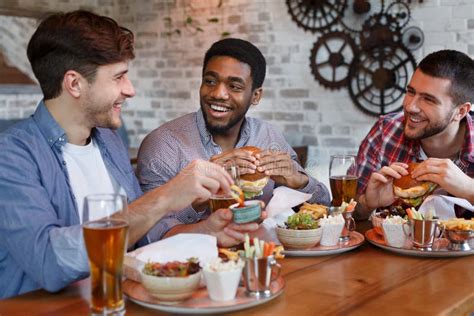 Friends Eating Burgers and Enjoying Beer, Sitting in Bar Stock Image ...