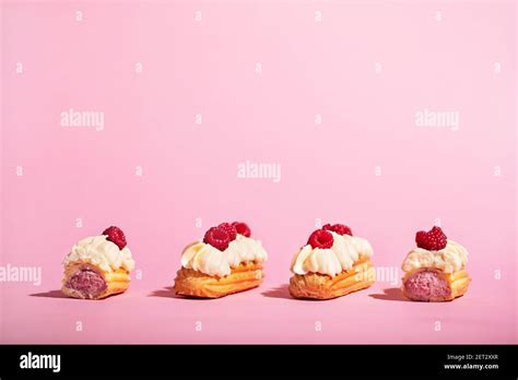 Four colorful eclairs with raspberries on pink background. Tasty sweet snack. French cuisine ...