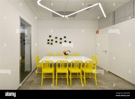 Large rectangular white wooden dining table surrounded by yellow chairs with fluorescent lights ...