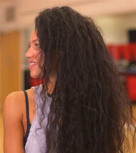 a woman with long, curly hair standing in a gym looking to the side and ...