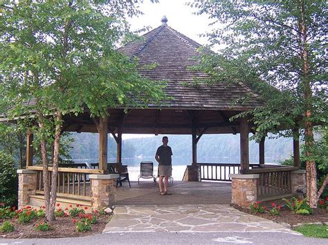 a man standing under a wooden gazebo next to flowers and trees in front of a body of water