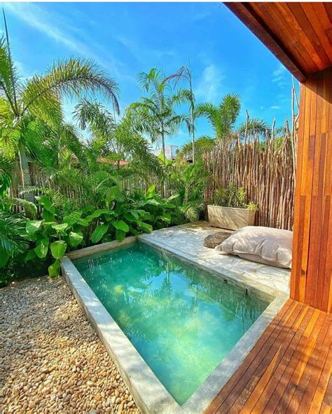 an outdoor swimming pool surrounded by greenery and wooden fenced in area with pillows on the side