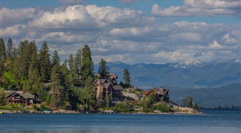 a lake with houses on it and mountains in the background, surrounded by pine trees