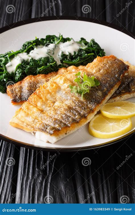 Grilled Sea Bass Fillet with Spinach Garnish in a Creamy Sauce Closeup on a Plate. Vertical ...