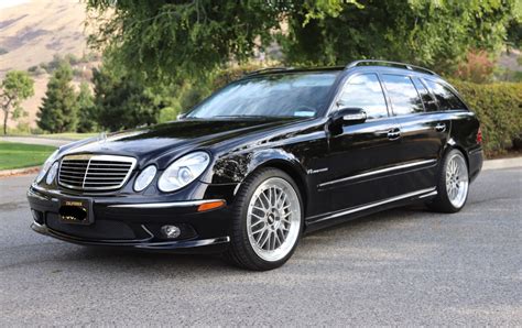 a black car parked on the side of a road next to some bushes and trees