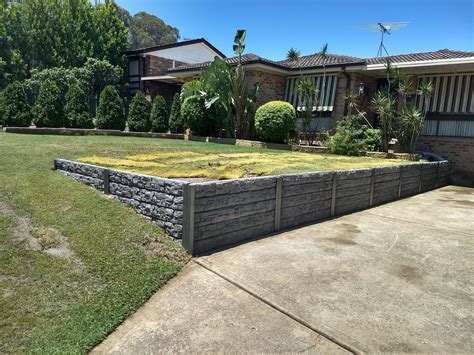 a stone retaining wall in front of a house with grass and bushes on the side