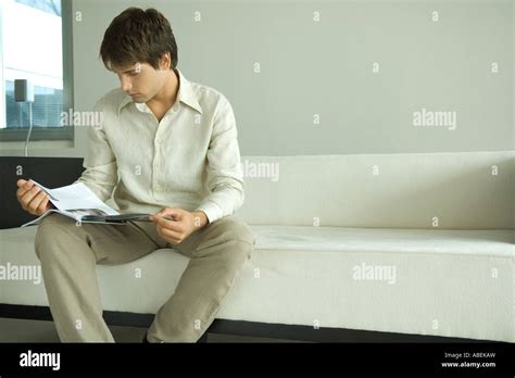 Man sitting on sofa reading magazine Stock Photo - Alamy