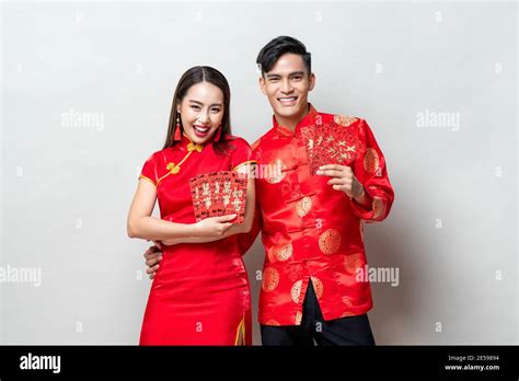 Happy Asian couple in traditional oriental costumes holding red envelopes or Ang Pao in light ...