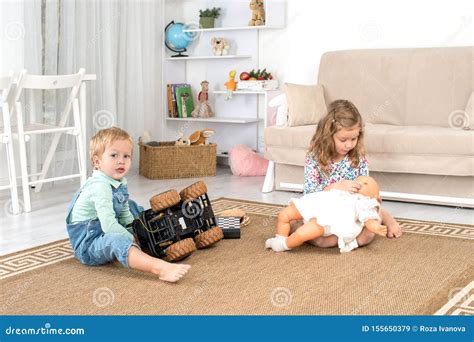 Little Children Sit on the Floor on a Rug in the Room at Home and Play with a Toy Car and a Doll ...