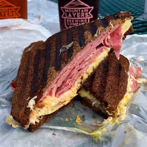 two halves of a ruben sandwich with pumpernickel bread stacked on top of each other with a beer ...