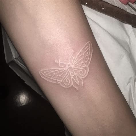 a small white butterfly tattoo on the arm