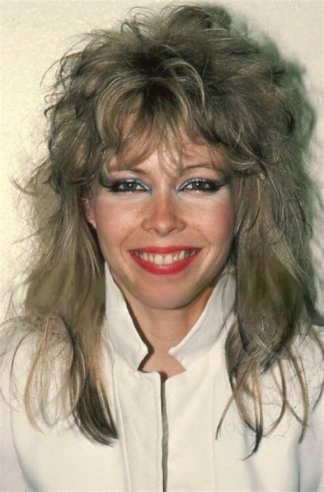 a woman with long blonde hair and blue eyes smiles at the camera while wearing a white shirt