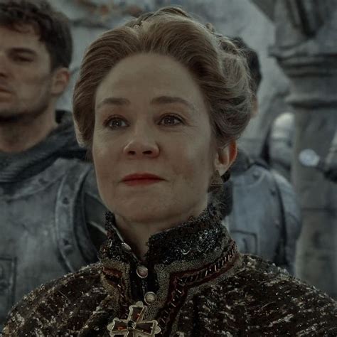 an older woman standing in front of a group of men with armor on their backs