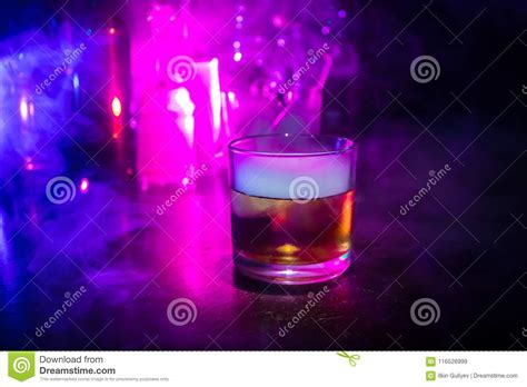 Glass of Whisky on Wooden Bar Closeup with Bottles Blurred View on Dark Background with Light ...