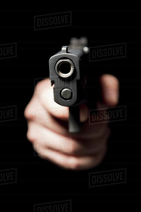 A hand holding a gun and pointing it at the camera, black background - Stock Photo - Dissolve