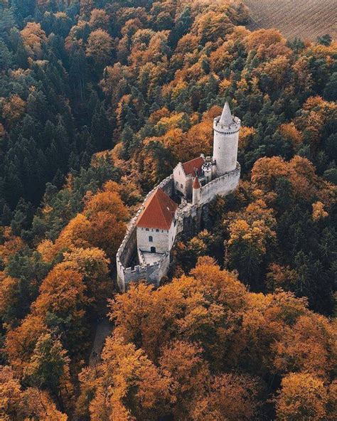 an aerial view of a castle surrounded by trees in the fall with orange and yellow leaves