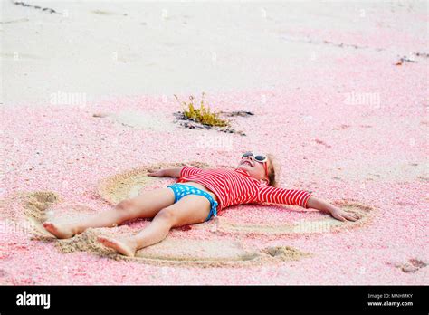 Little girl making sand angel on beautiful pink sand beach at tropical island of Barbuda in ...