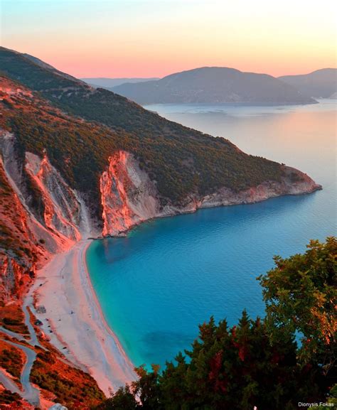 an aerial view of the blue water and beach at sunset with mountains in the background