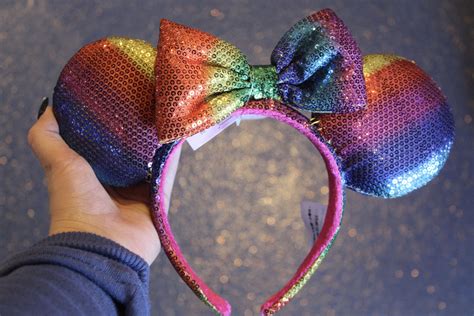 a person is holding up a colorful minnie mouse ears headband with sequins