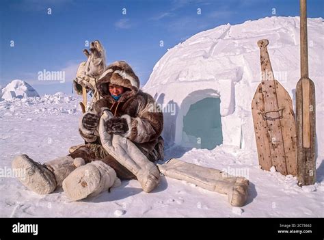 Woman inspects hand sewn boot liners made of caribou skin while sitting outside igloo. She is ...