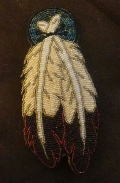 an embroidered brooch with feathers and a cross on the top, sitting on a black surface