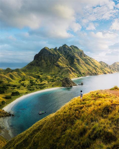 a man standing on top of a lush green hillside next to a body of water