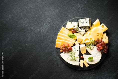 Cheese platter with craft cheese assortment and grape at black background. Top view with copy ...