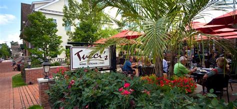 people sitting at tables in front of a restaurant with red umbrellas ...